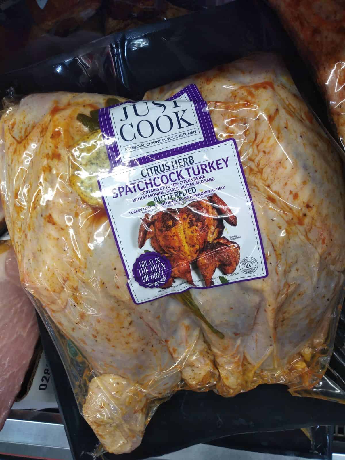 Just Cook brand Citrus Herb Spatchcook Turkey in clear packaging. You can see the lemon and seasoning. 