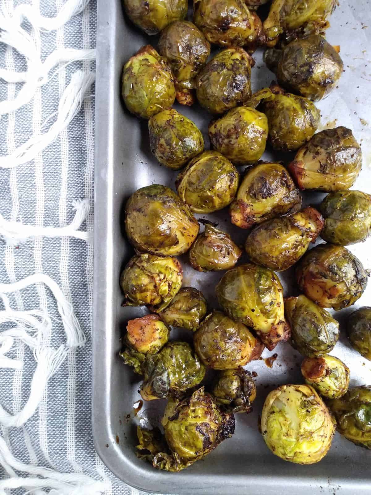 Whole sous vide brussels sprouts that have been browned in the oven on a metal sheet pan with a gray and white strip towel under the pan. 