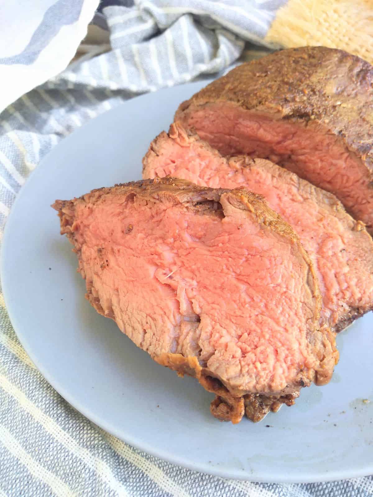 Slice of medium cooked beef tenderloin on a blue plate on a gray and white striped towel