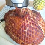 A bone-in ham on a cutting board that has been cooked in the Instant Pot along with pineapple juice and brown sugar.