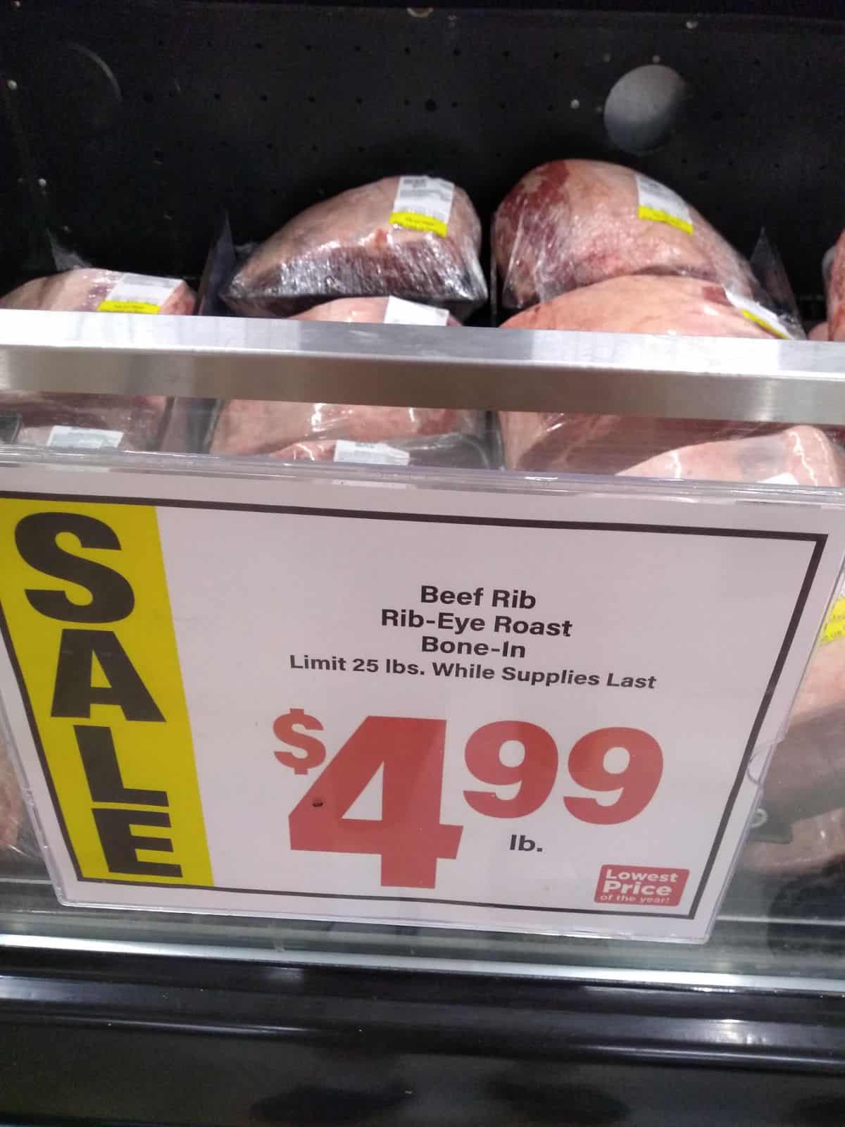 A grocery store beef display with a sign that reads "Beef Rib Rib-Eye Roast Bone-in Limit 25 lbs. While supplies last. $4.99/lb."