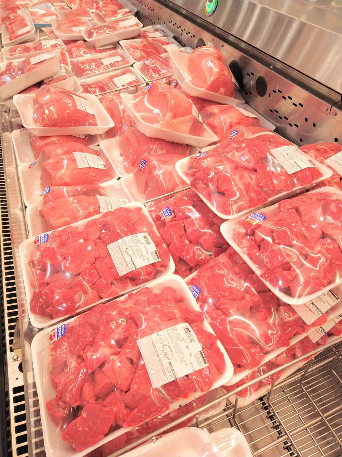 A Costco display of Choice meats in a refrigerated case. Packs of meats are wrapped in plastic. In front is stew meat with other roasts in the background.