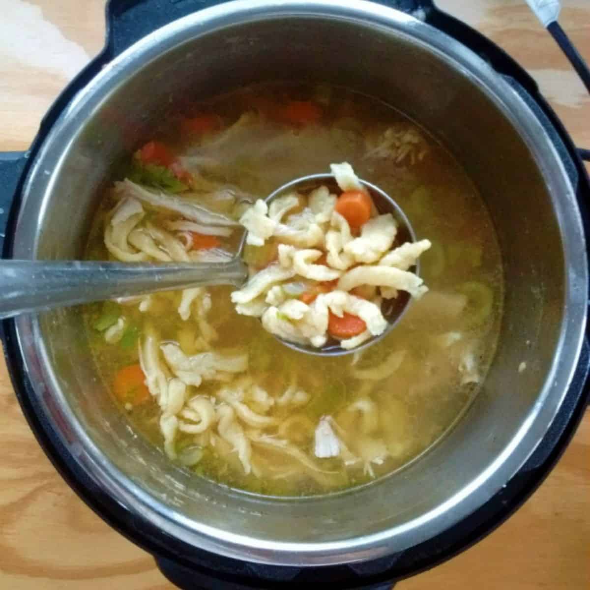 An Instant Pot full of chicken noodle soup with homemade noodles and carrots. A ladle is hanging above the pot showing you a closer look at the contents of the soup.