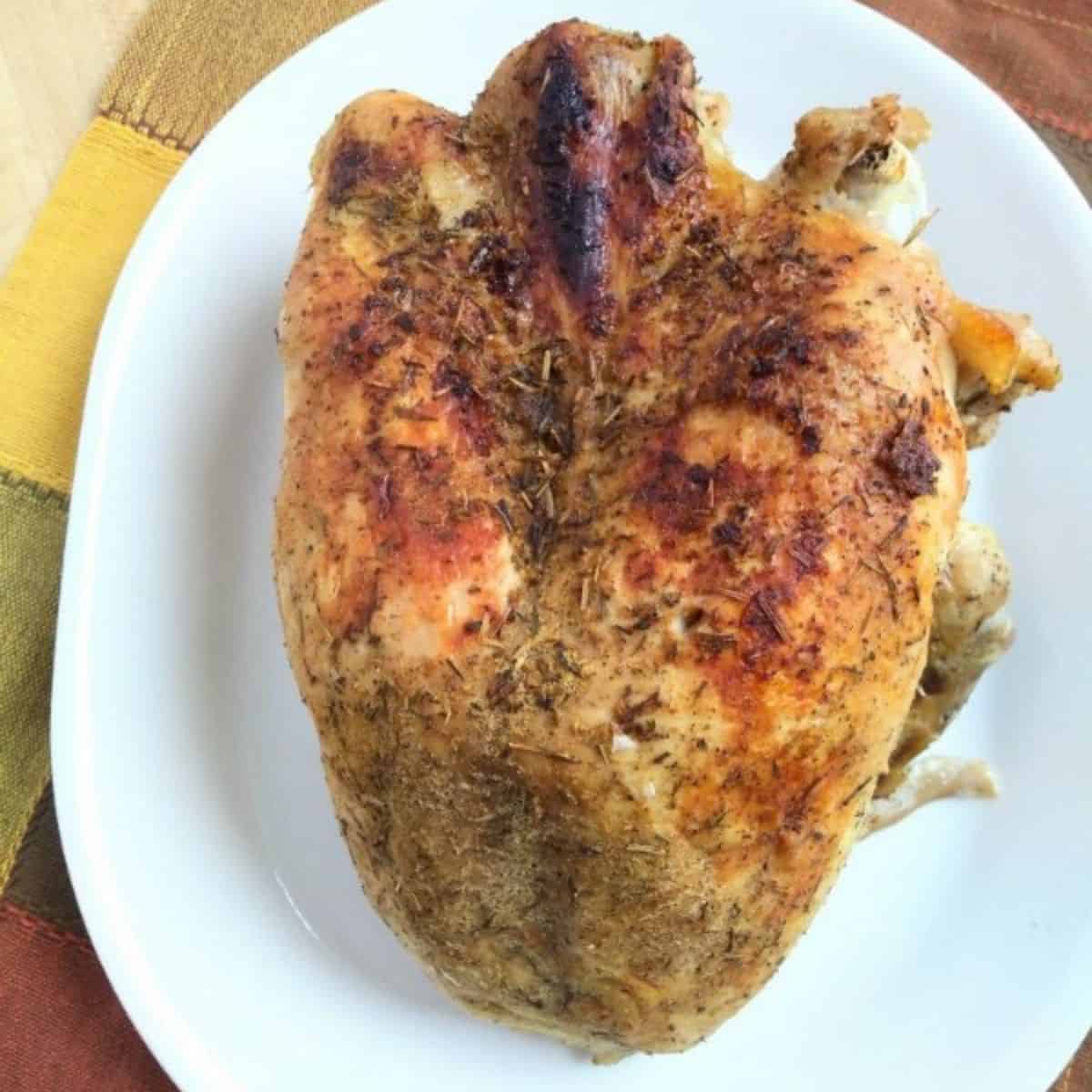 A browned turkey breast sitting on a white platter on top of a green, yellow, and red plaid towel.