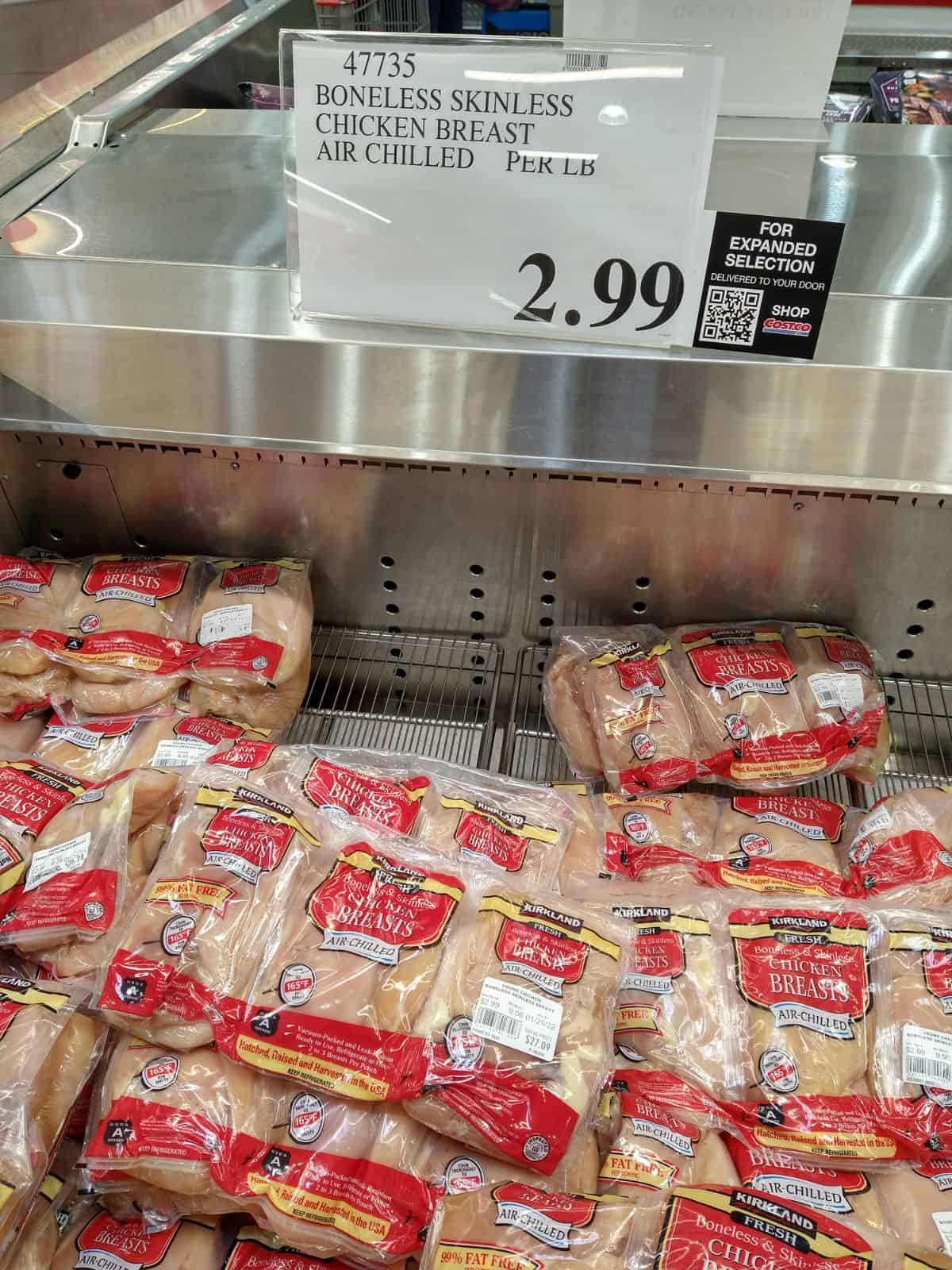 Kirkland Boneless Skinless chicken breasts in packaging in refrigerated display at Costco. A sign shows the chicken costs $2.99/lb.