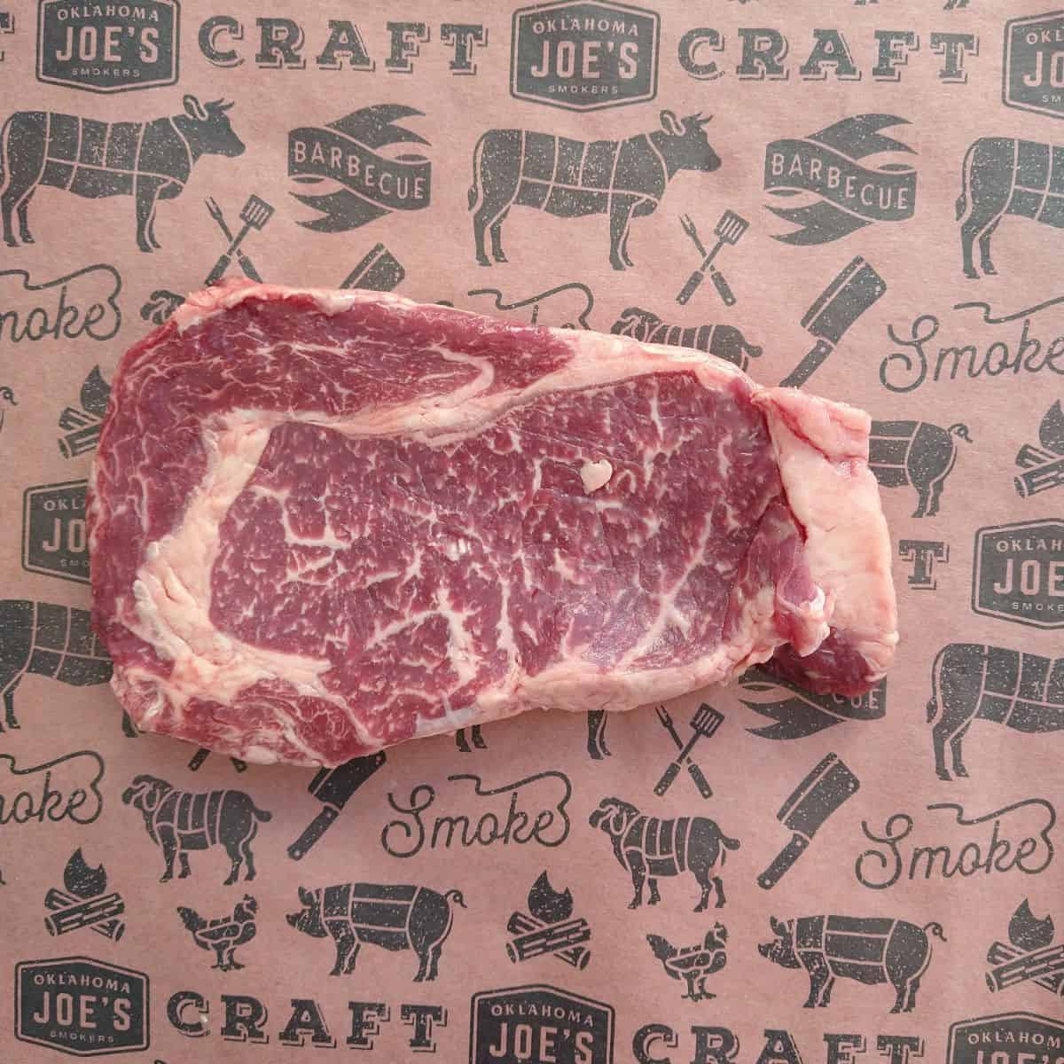 A single Rib eye steak with a lot of marbling on a piece of reddish brown butcher paper