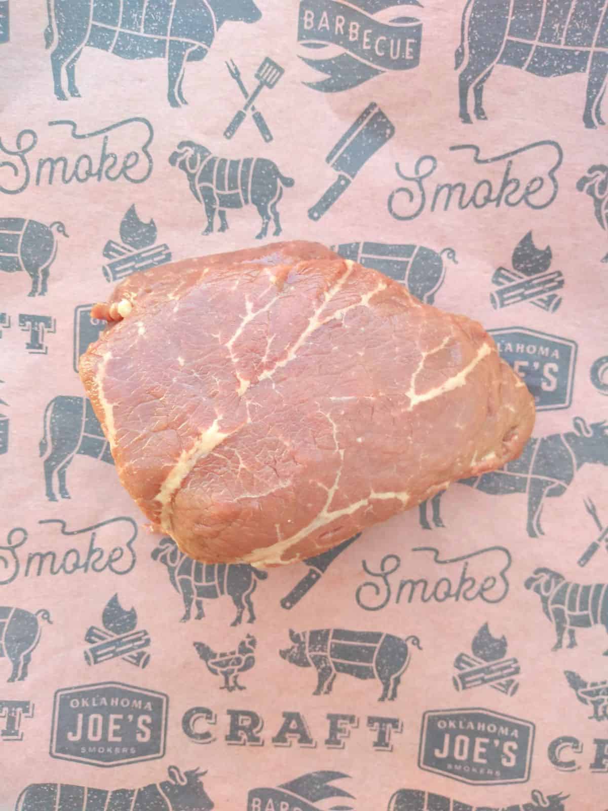 A raw top sirloin filet steak on a piece of buttering paper with grilling symbols on it. The picture shows a close up of the marbling of fat within the steak. 