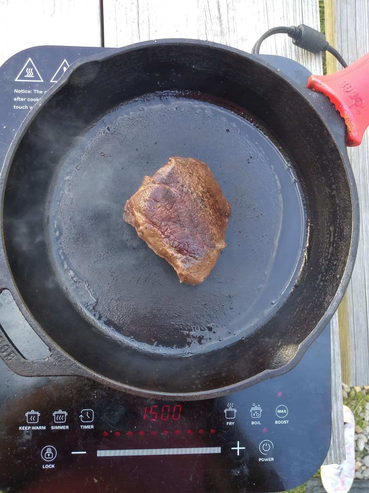 A sirloin filet steak in an oiled cast iron pan on top of an induction cooktop