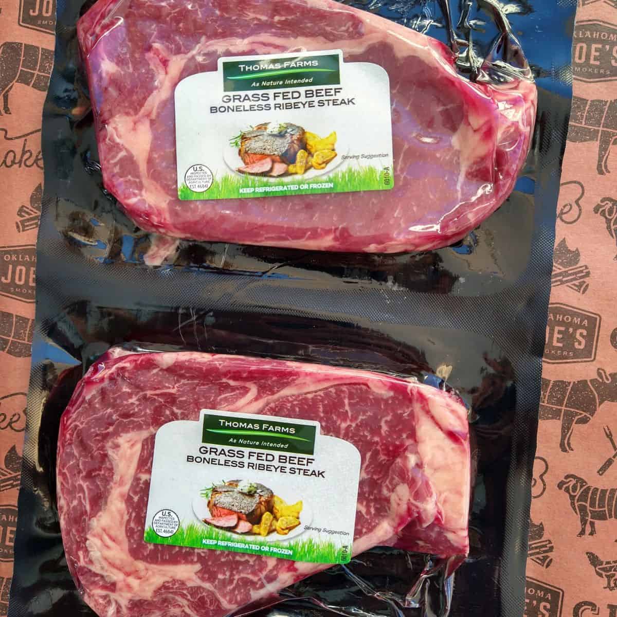 A two pack in packaging of Thomas Farms Grass Fed Beef Boneless Ribeye Steak from ALDI on a reddish brown sheet of butcher paper.