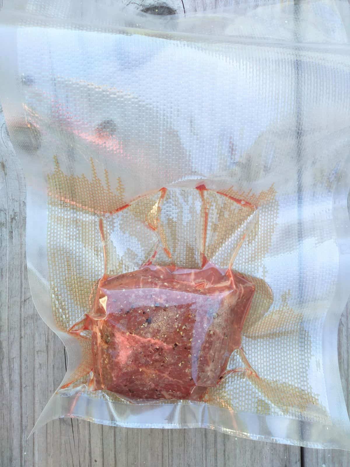 A vacuum sealed sirloin filet steak on a wood picnic table.