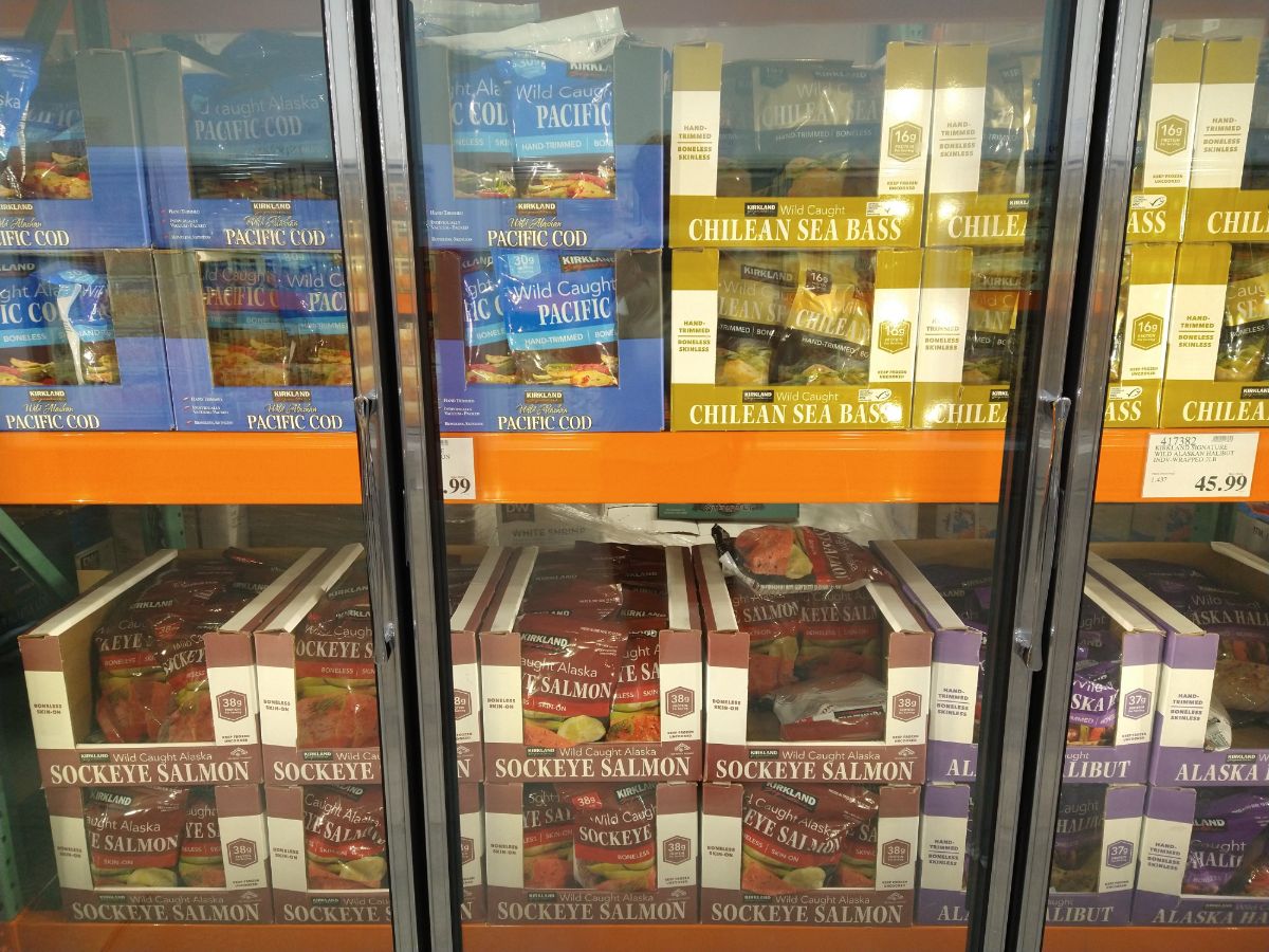 Boxes with bags of frozen fish in the freezer section at Costco. Fish includes pacific cod, Chilean sea bass, sockeye salmon, and Alaska halibut. 