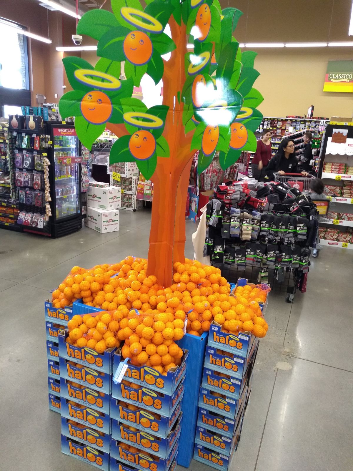 A carboard tree display at a grocery store with Halo mandarins in the tree and a box underneath with bags of them