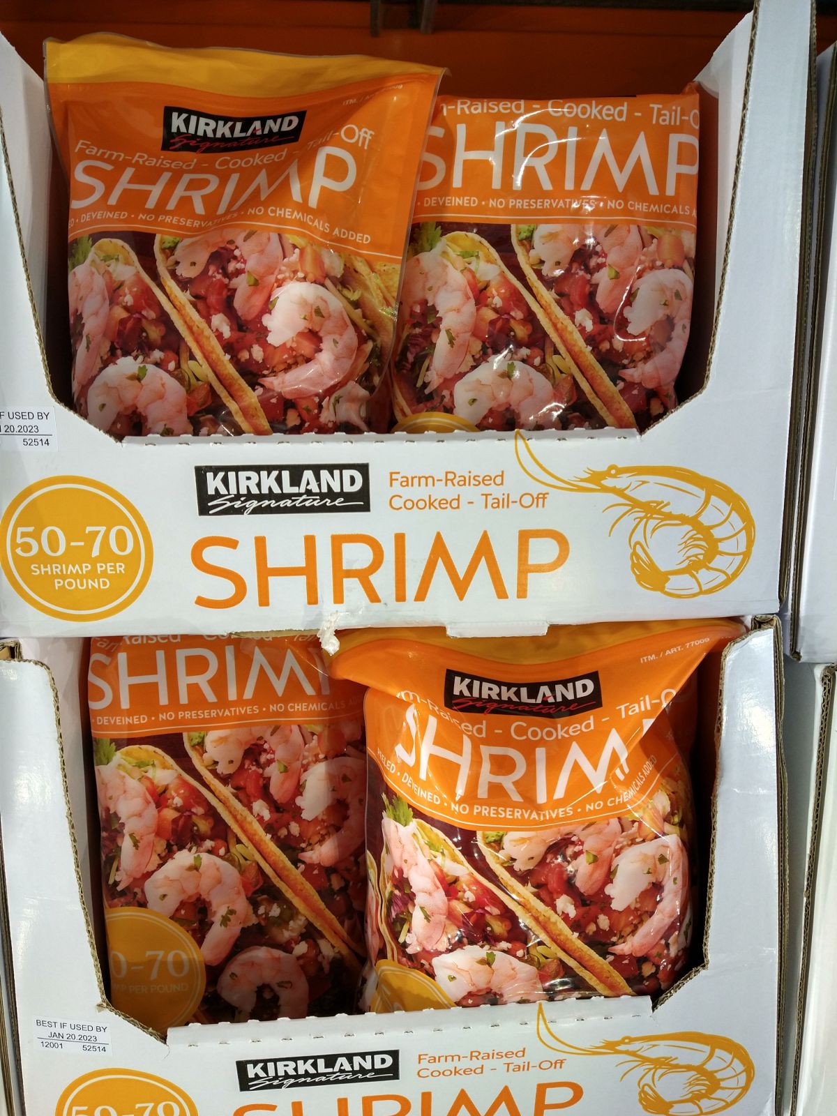 A box filled with orange bags of Kirkland Farm-Raised Cooked Tail Off shrimp.