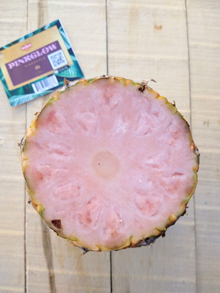 The top cut of a pink pineapple with the Del Monte pinkglow tag nearby on the table. You can see the inferior of the pineapple that is truly pink.