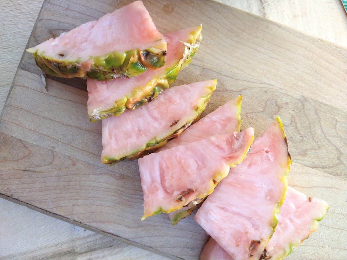 Slices of pink pineapple are arranged on a wood cutting board on top of an another wood board.