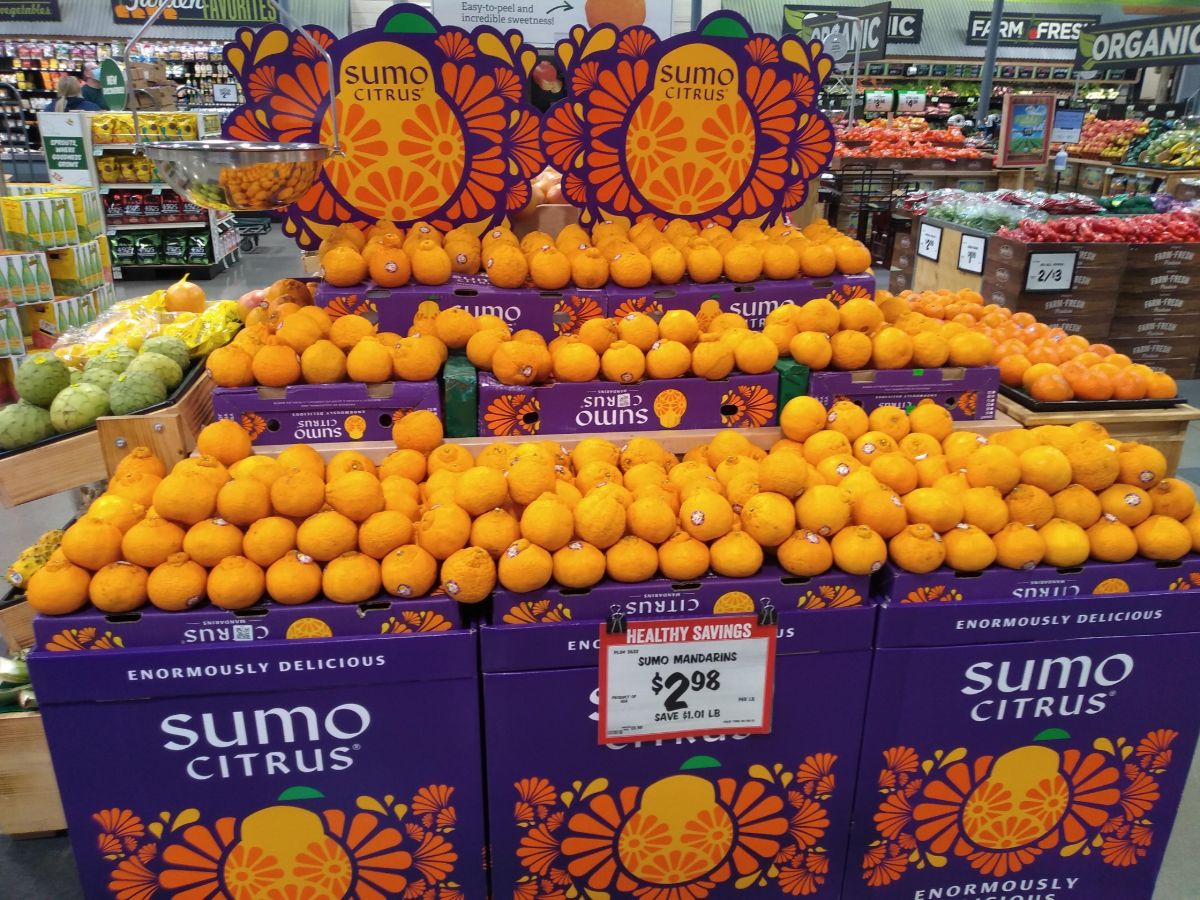 A huge display of Sumo Citrus mandarins with purple colored boxes and several signs advertising the fruit at a Sprouts store.