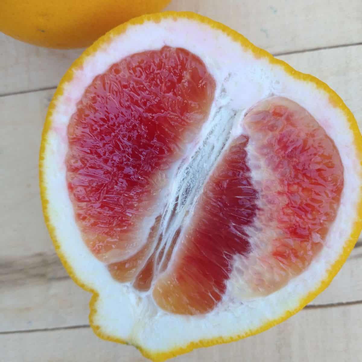 A sliced open Valentine Pomelo showing the red interior sitting on a wood board.