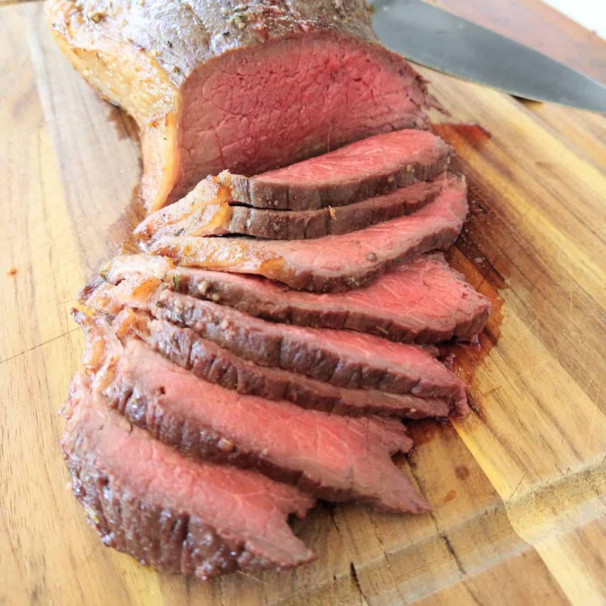 A sliced bottom round roast cooked to medium rare sitting on a wood cutting board.