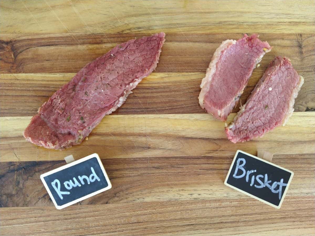 Cooked slice of cooked beef round on a cutting board next to slices of cooked corned beef brisket. 