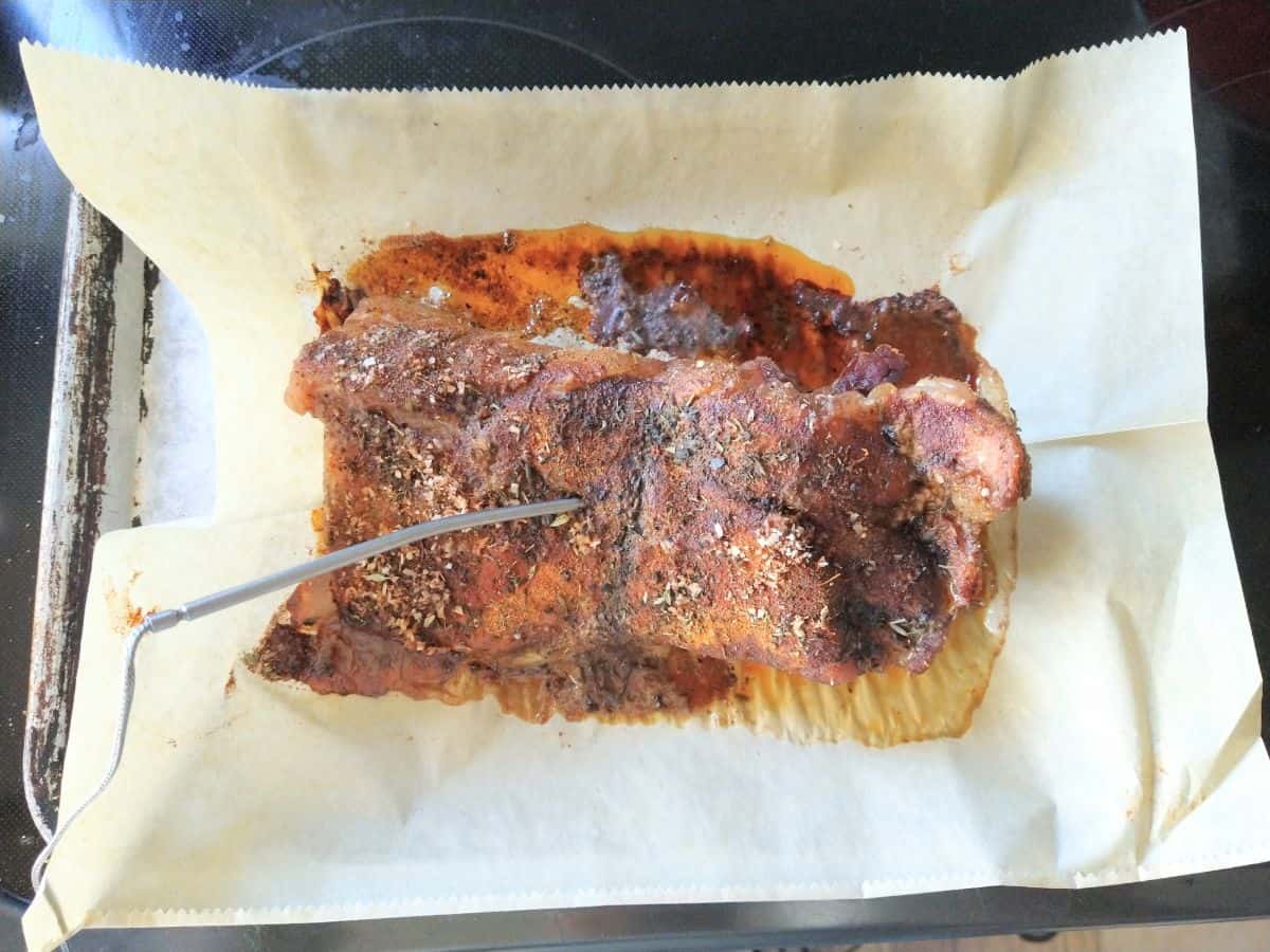 Cooked pork brisket on a parchment lined sheet pan with a probe from a thermometer stickling into the meat.