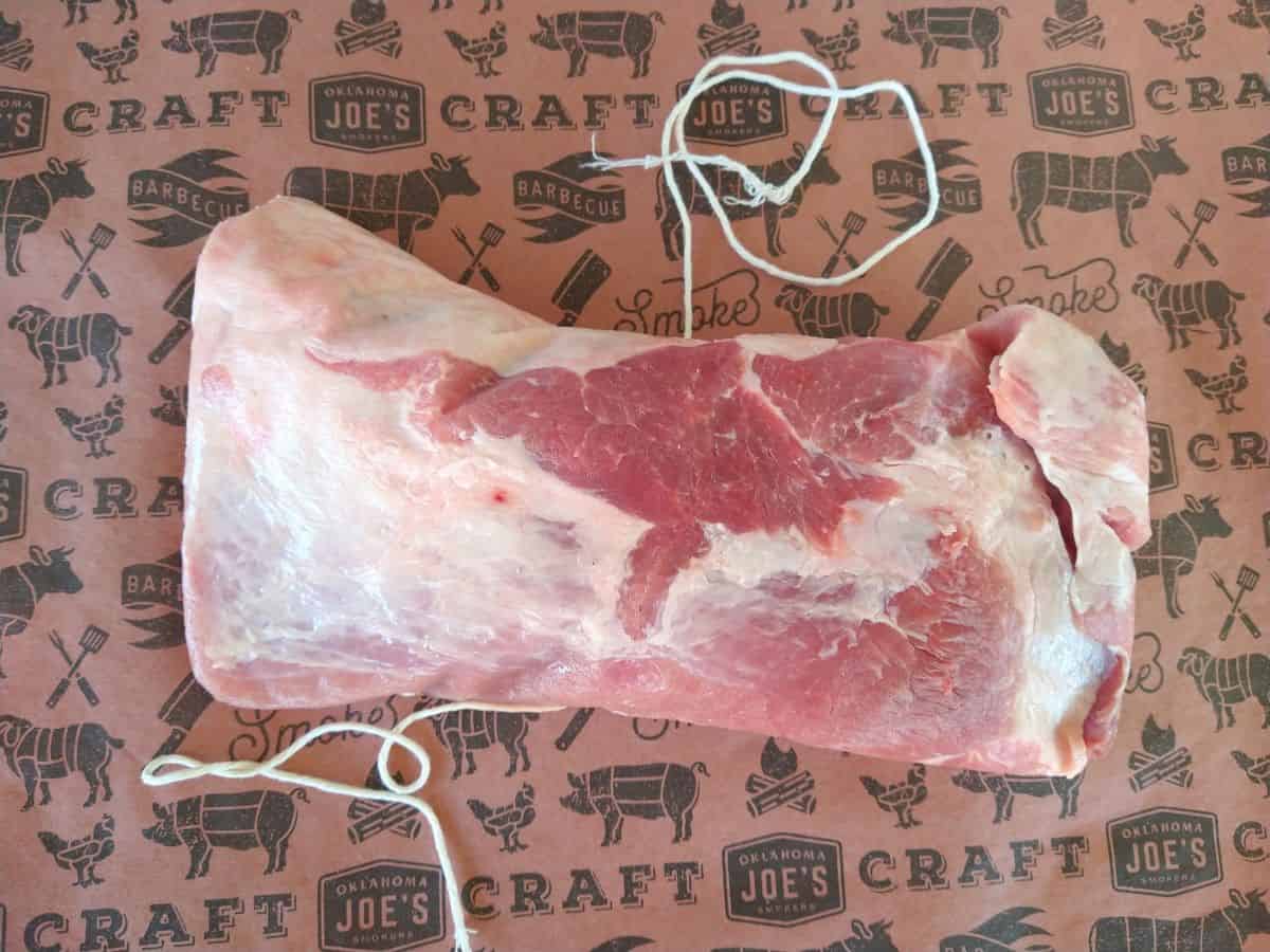 A raw pork brisket sitting on a piece of butcher paper with butcher string underneath the meat.