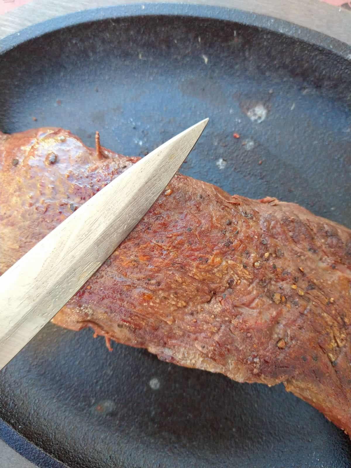 A Teres Major steak in a cast iron skillet with a knife showing how to cut against the grain.