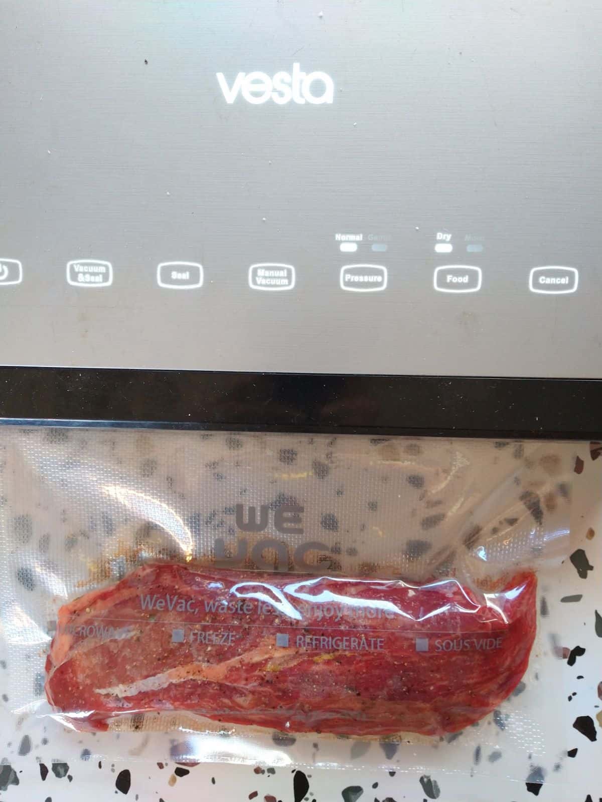 A Vesta vacuum sealer with a Teres Major steak in a bag being sealed on a table.