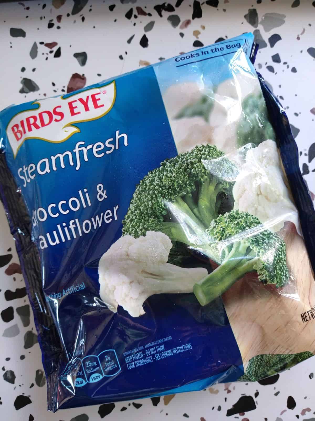 A bag of Birds Eye Steamfresh broccoli and cauliflower sitting on a white and dotted table. 