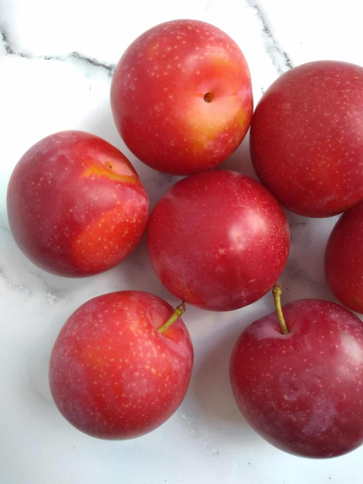 Cherry and plum hybrid sitting on a white background. They are red in color with spots.