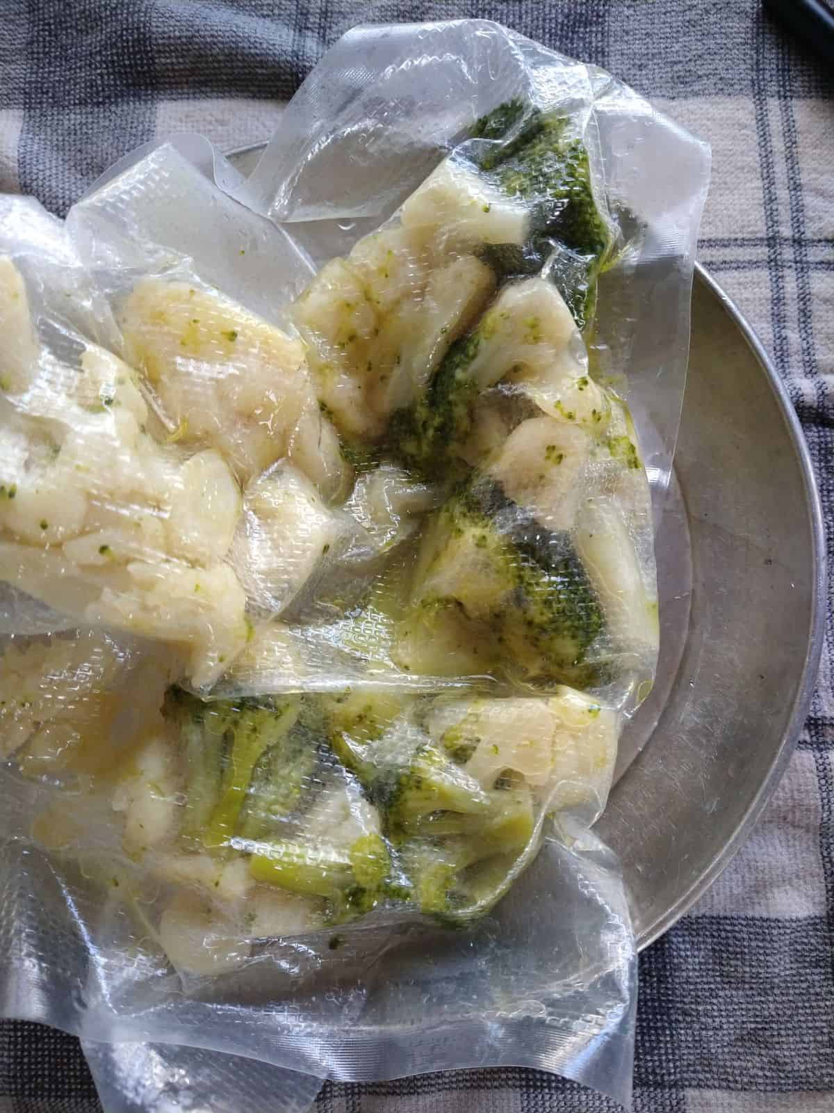 Sous vide broccoli and cauliflower still in the bag on a metal camping plate with a gray and white towel underneath. 