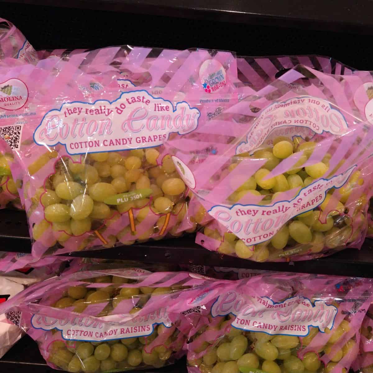 A display of green colored Cotton candy grapes at the grocery store. The bags say "They really do taste like cotton candy" on them. 