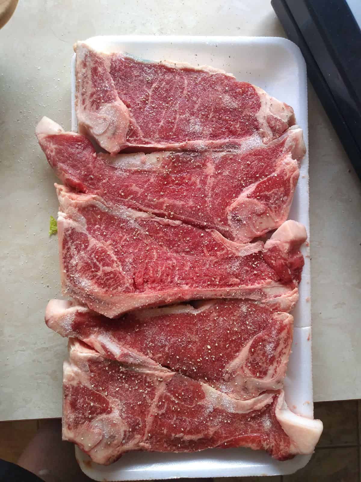 New York strip steaks in an opened package with 4 steaks in them. The steaks are covered in kosher salt.