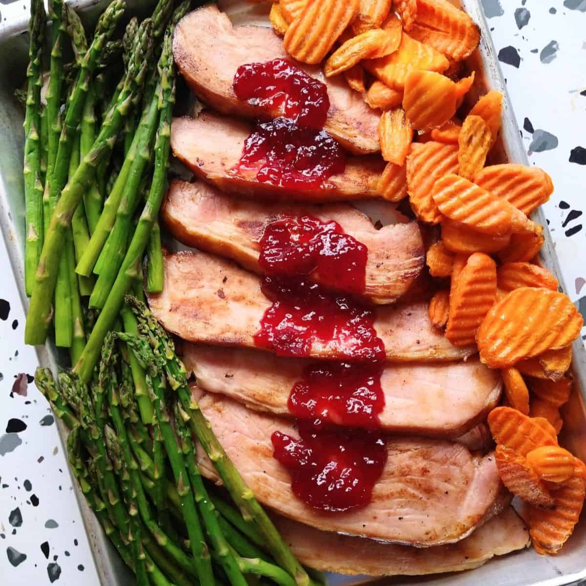 A sheet pan with asparagus, ham with glaze, and crinkled cut carrots.