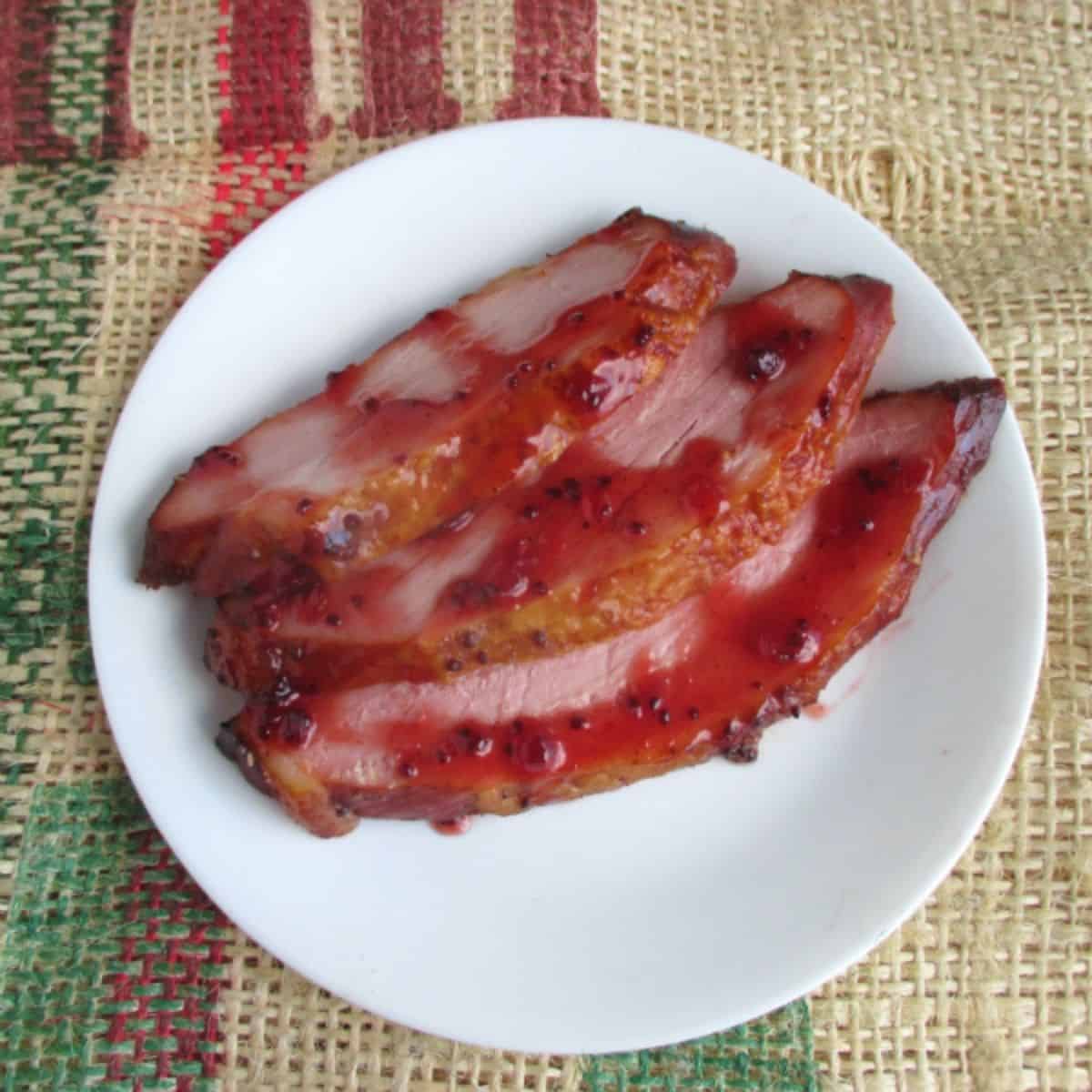 Slices of Kirkland Master Carve ham  on a white plate with homemade red currant glaze on top. The plate is sitting on a piece of burlap.
