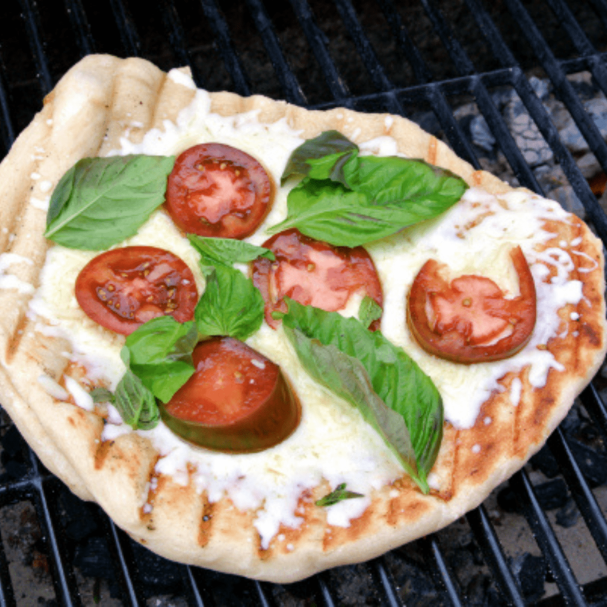 Margherita Pizza with mozzarella, basil, and tomatoes on a grill. Grill marks can be seen on the crust.
