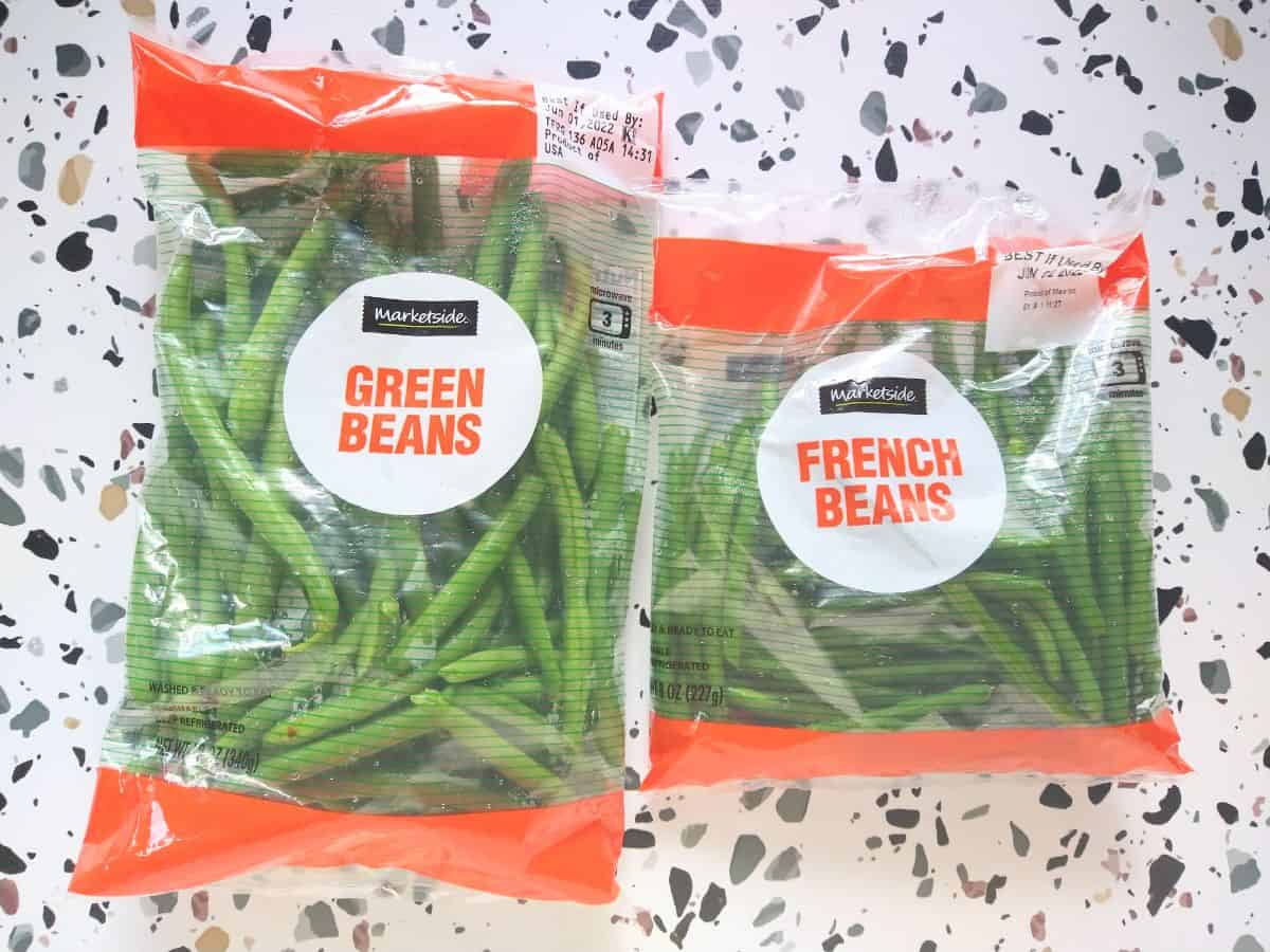 A bag of Marketplace green bags from Walmart on the left, next to a bag of French Beans both sitting on a white table with colored spots.