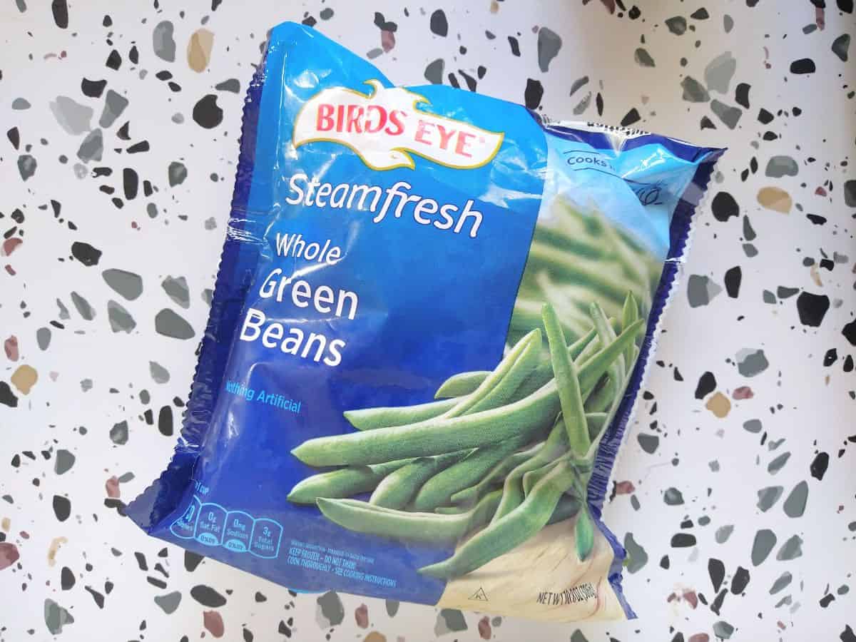 Frozen Birds Eye Steamfresh Whole green beans sitting on a white table with colored spots. 