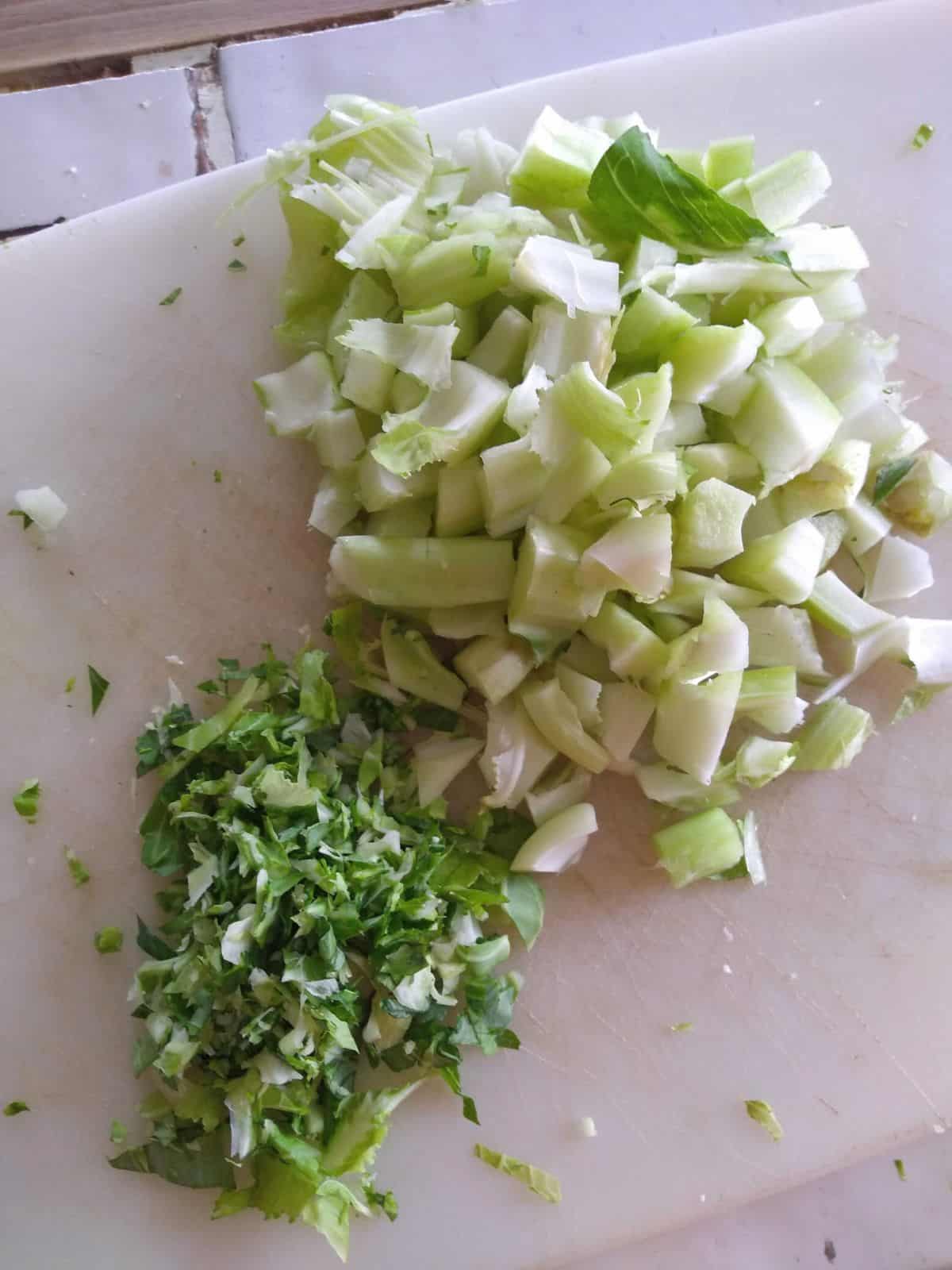 Chopped cauliflower stems and leaves on a white plastic cutting board.