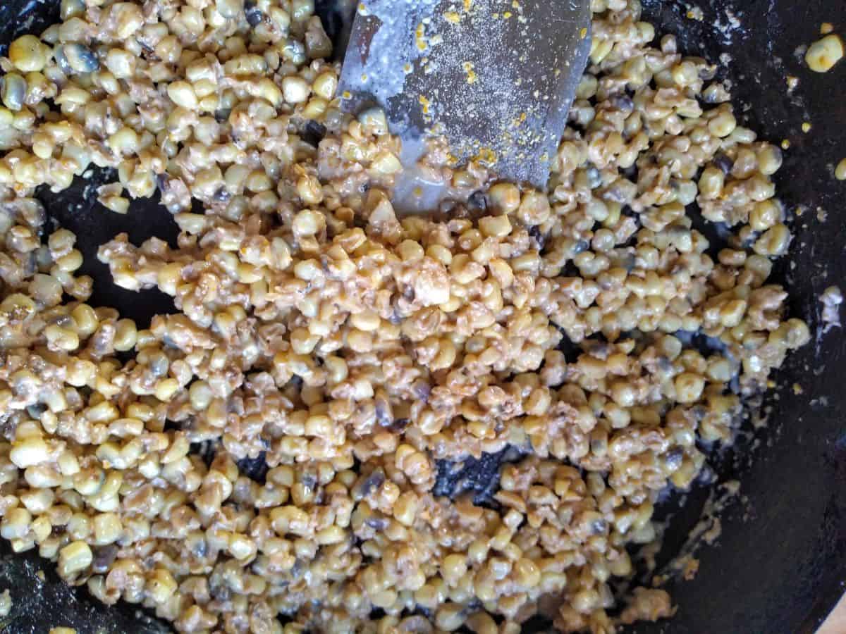 Corn in a cast iron skillet being stirred with a metal spatula.
