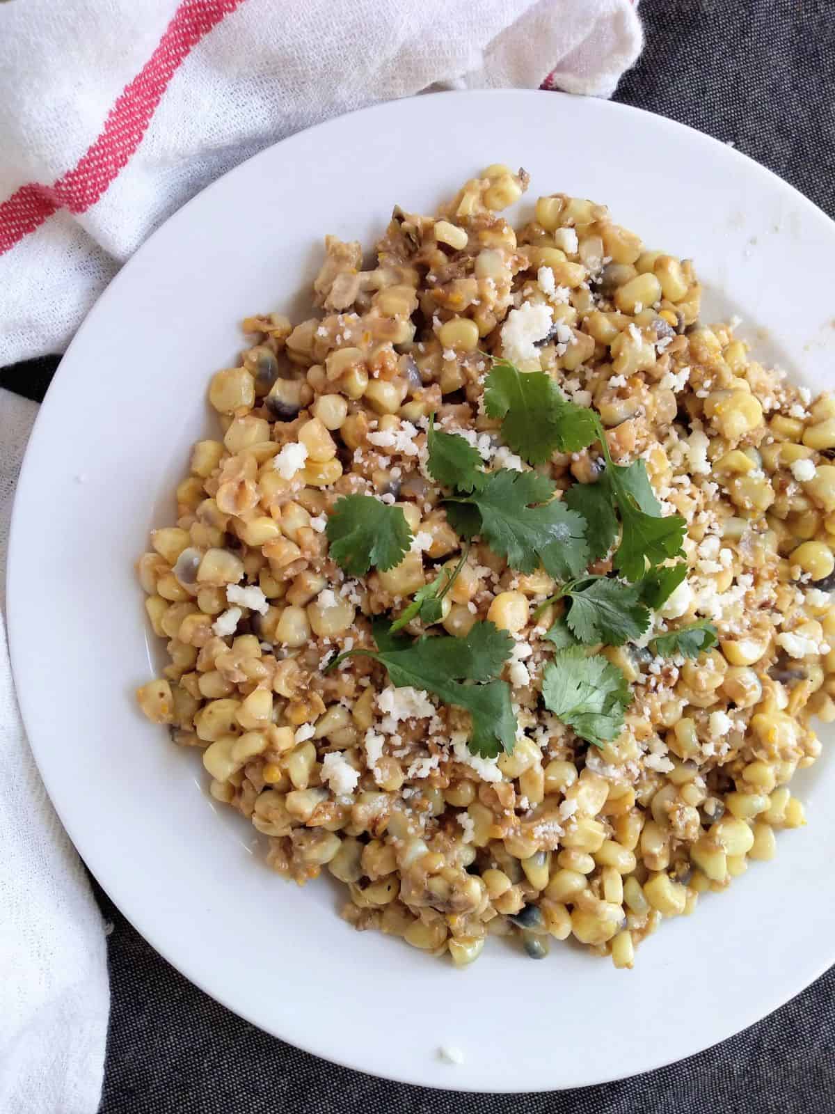 Elote Mexican Street Creamed Corn on a white plate topped with Cotija cheese and cilantro