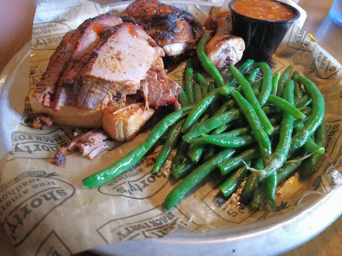 A plate of BBQ meat, baked beans, and green beans that are front and center.