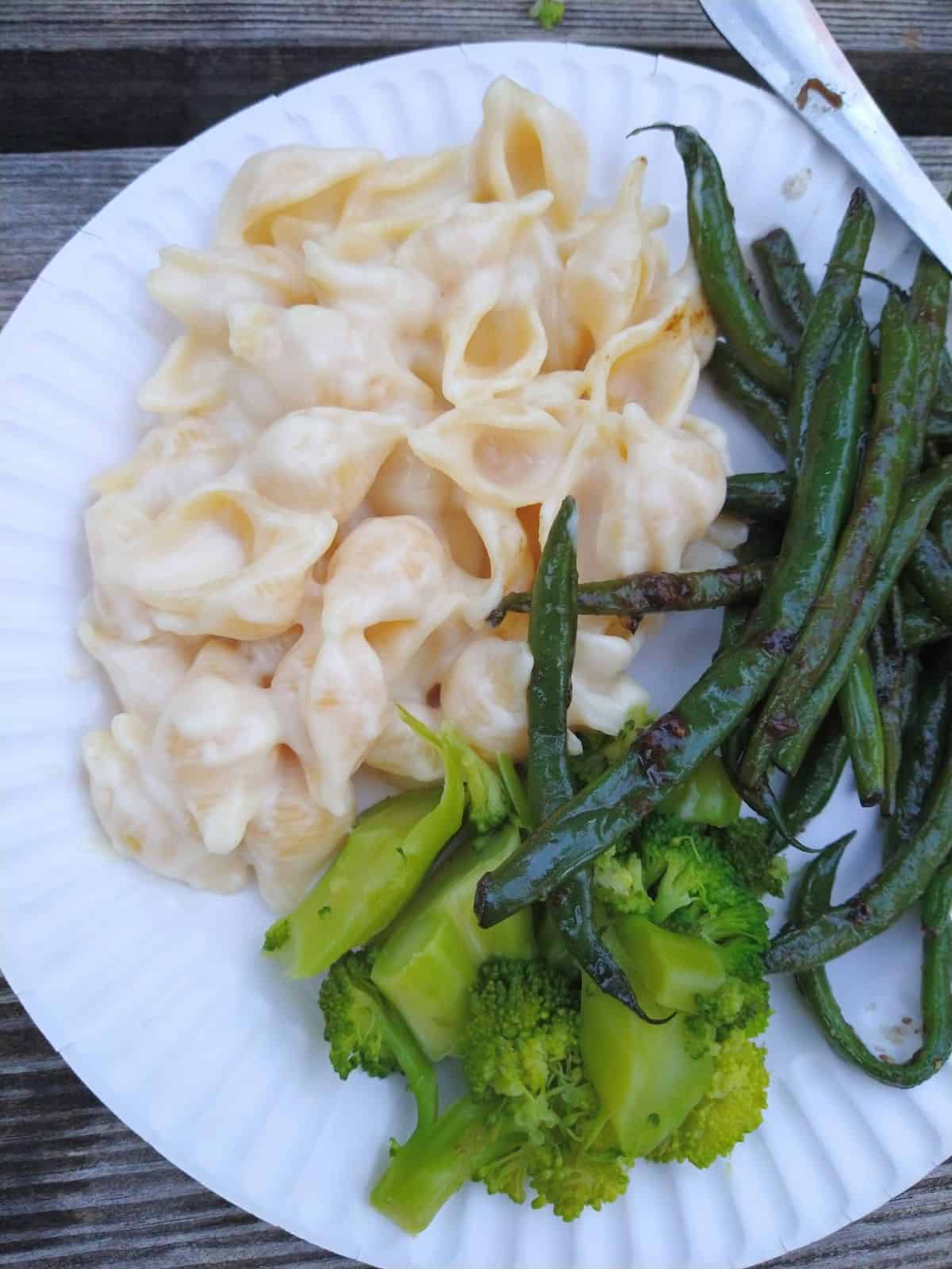 A paper plate with shells & cheese, green beans and broccoli.
