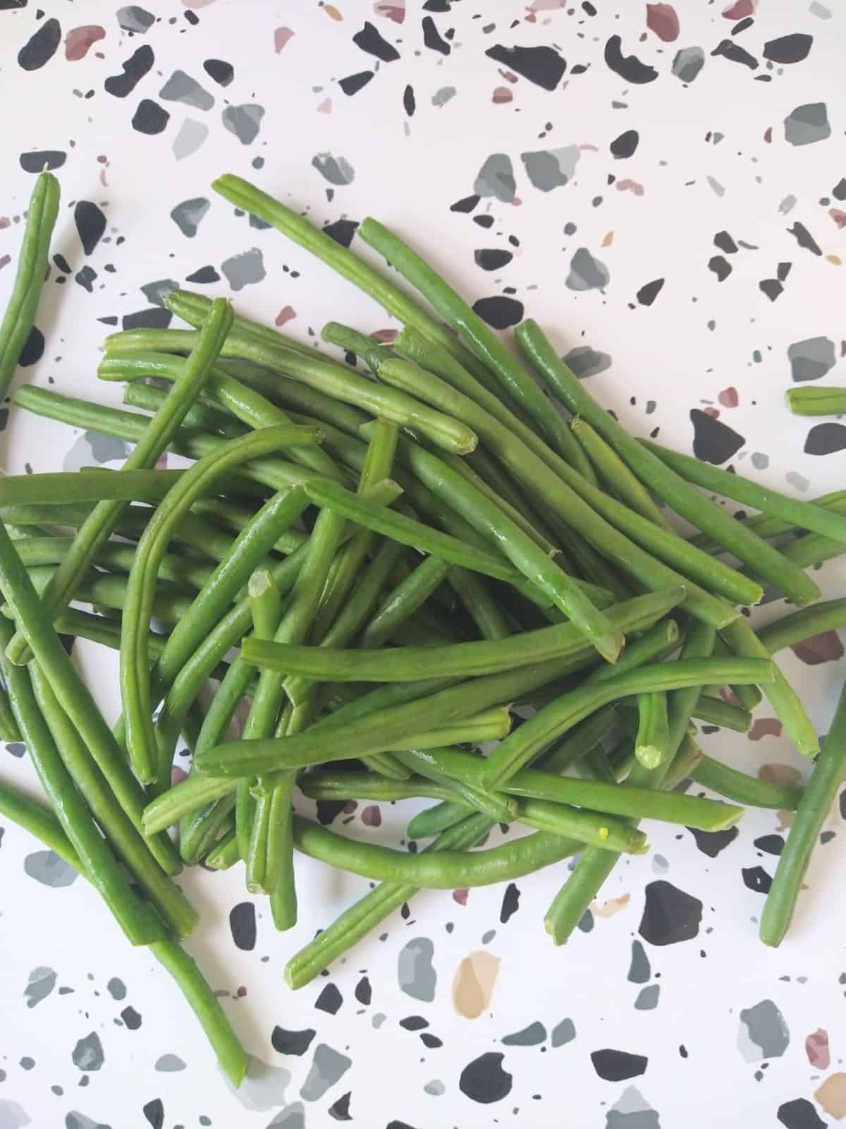 Raw French beans on a table that is white with gray, black, and brown spots.