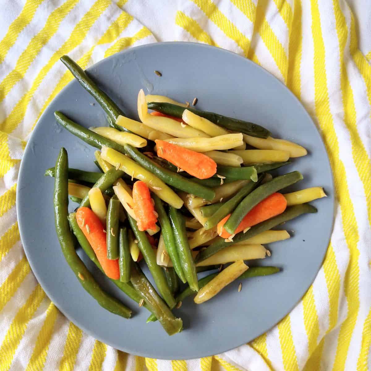 A plate of green beans, wax, beans, and baby carrots on a white and yellow striped towel.