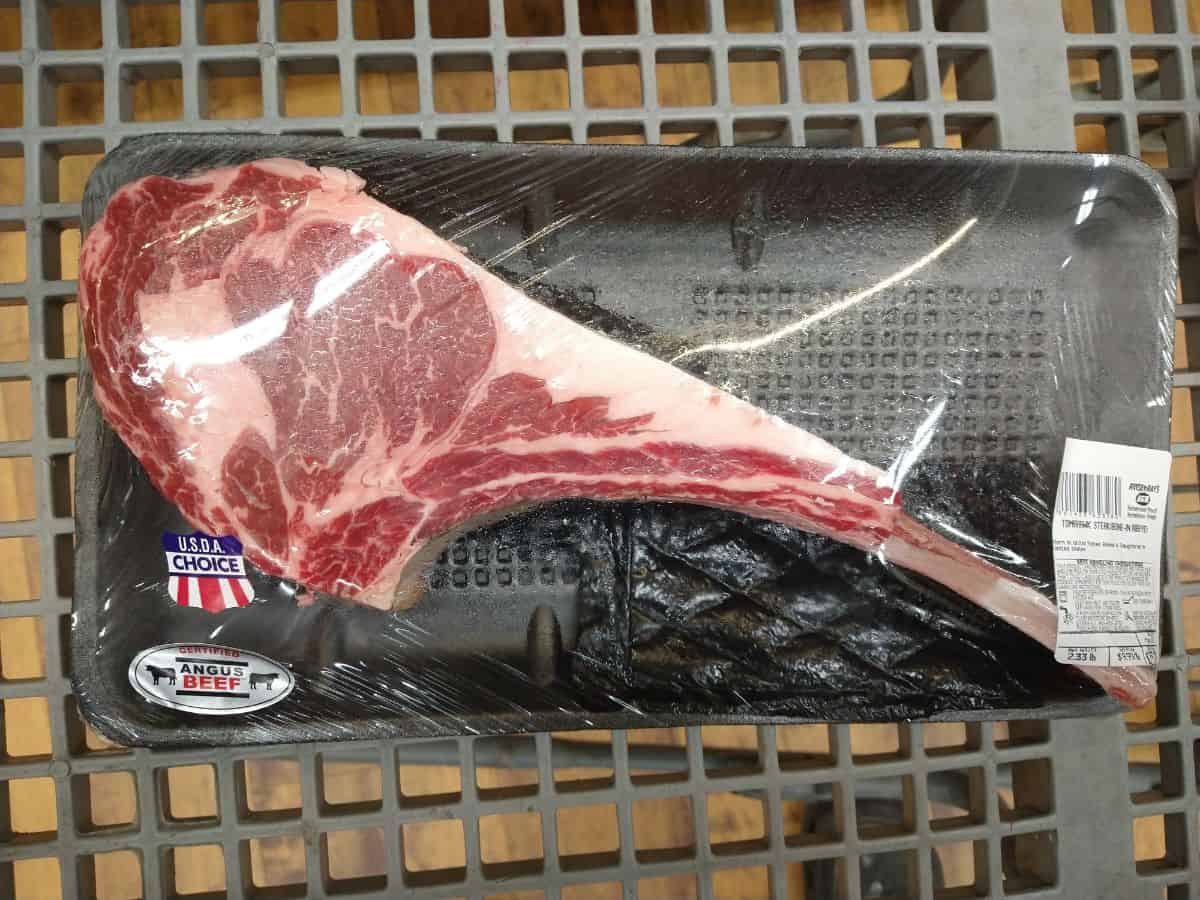 A USDA Choice Tomahawk Ribeye steak in a package in a grocery cart.