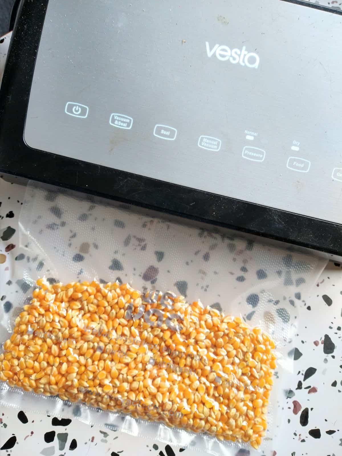 Vesta vacuum sealer being used to seal yellow popcorn kernels on in a plastic bag.