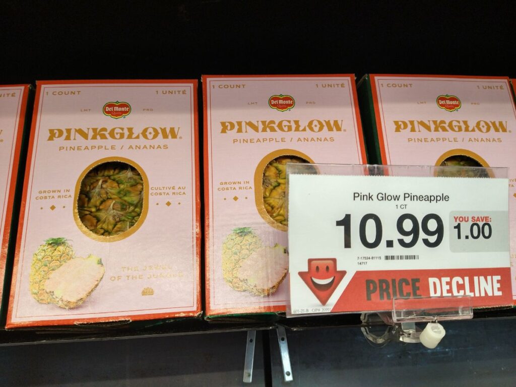 A display of Boxed Pinkglow Pineapples at a Hy-Vee store. A sign says they are $10.99 which is a price decline of $1.