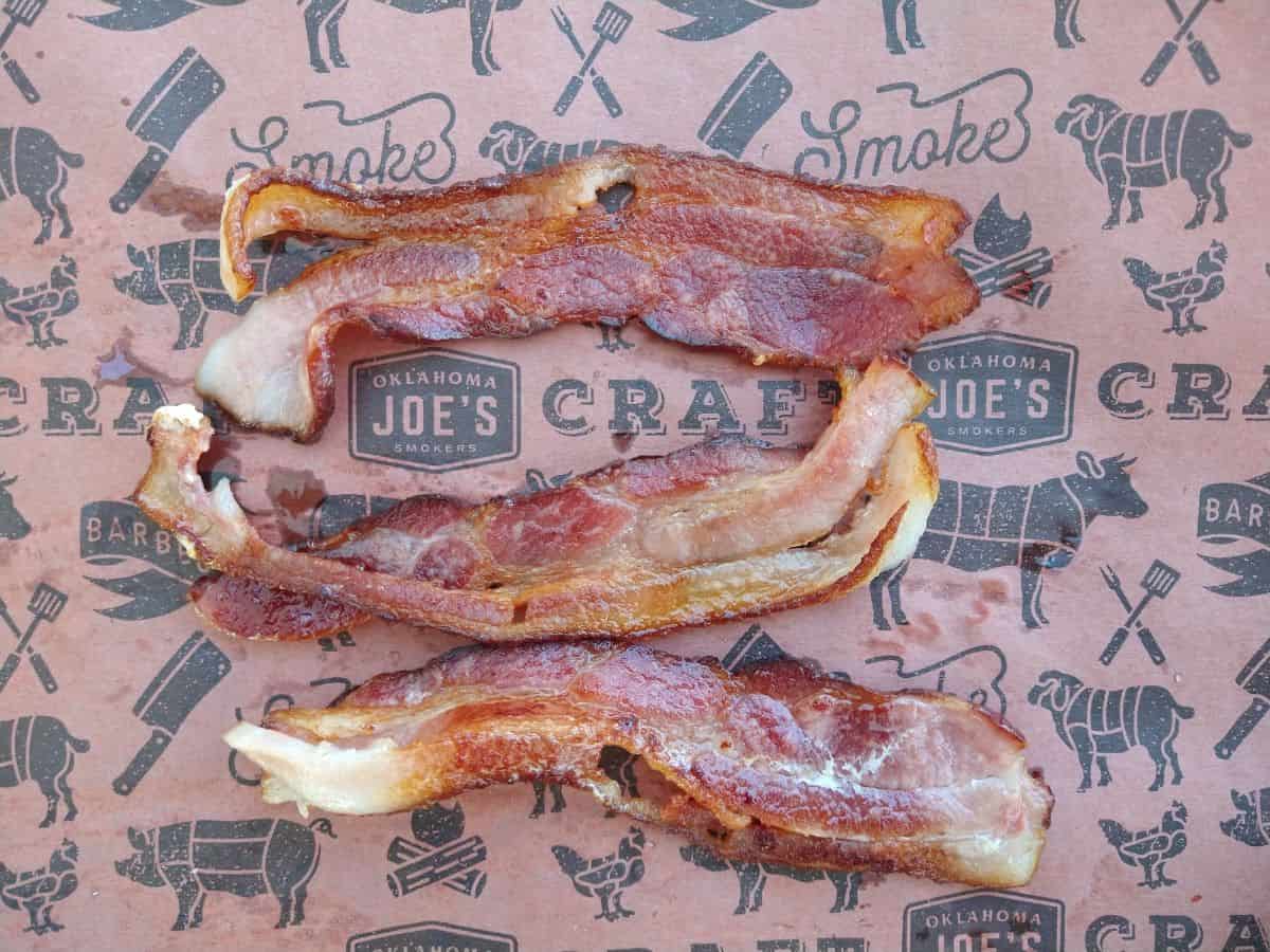 Three stirps of cooked bacon on a piece of butcher paper.