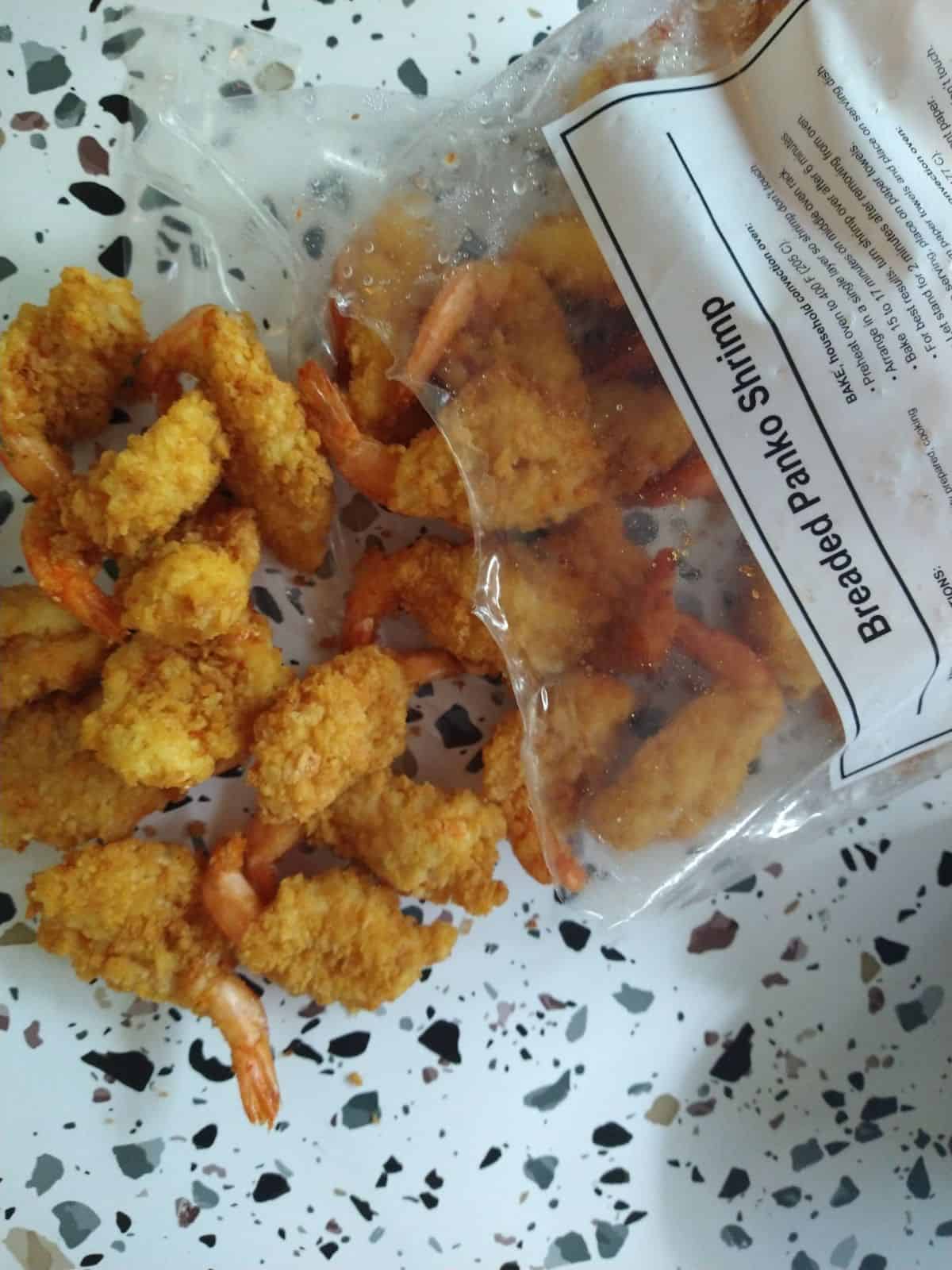 The bag of Kirkland Panko Fried Shrimp opened up and spilling onto a white table with colored spots.