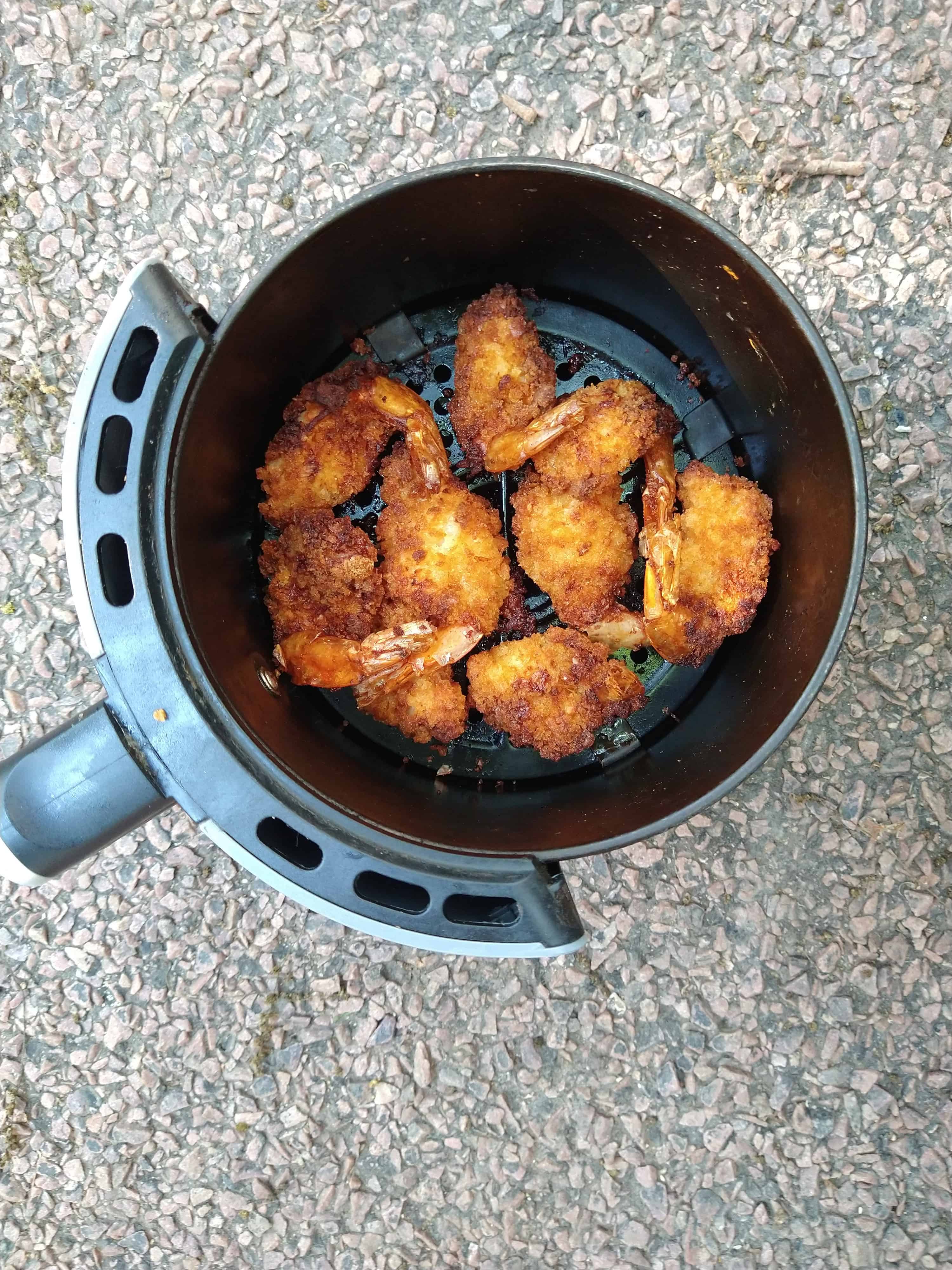 The basket of a black air fryer with cooked crispy fried shrimp inside. 